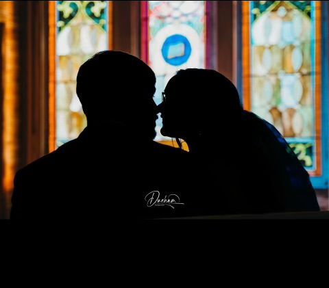 A silhouette of a man and woman kissing in front of a stained glass window.