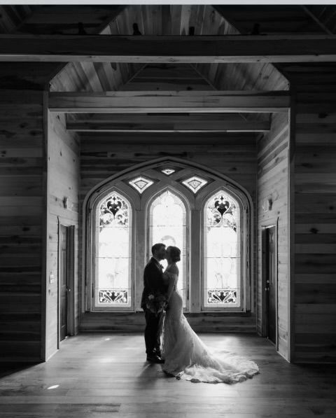 A bride and groom are kissing in front of a stained glass window.