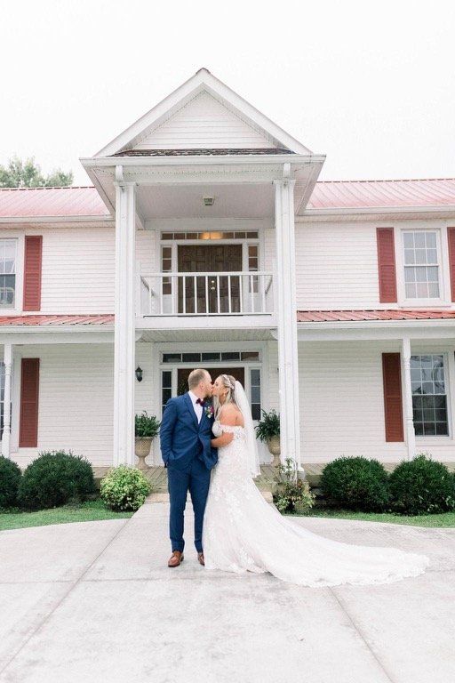 A bride and groom are kissing in front of a large white house.