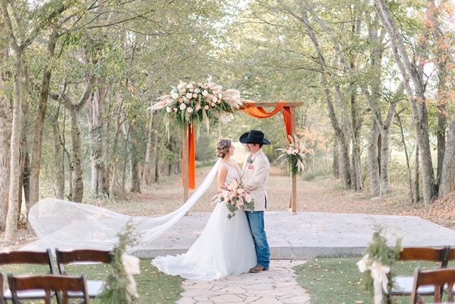 A bride and groom are posing for a picture at their wedding ceremony in the woods.