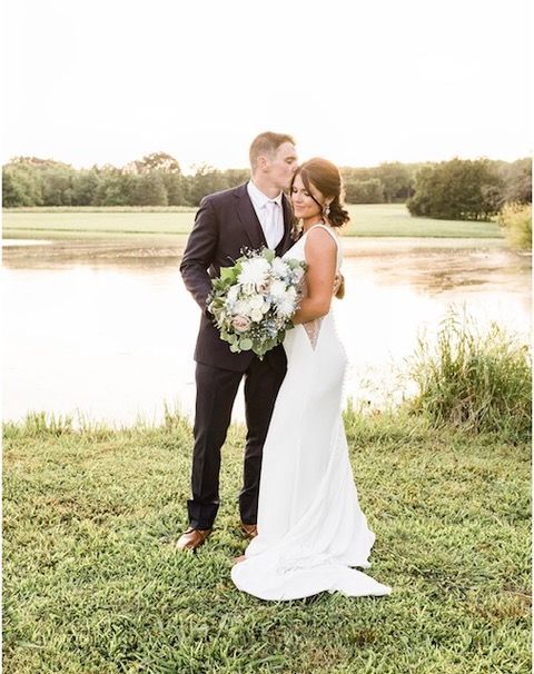 A bride and groom are kissing in front of a lake.