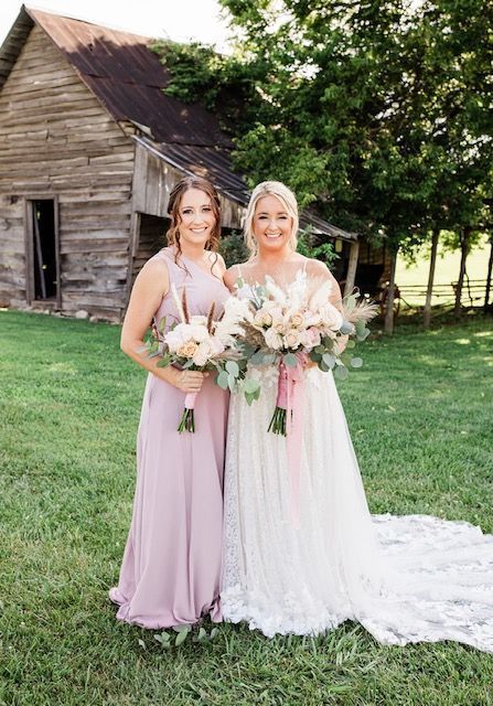 A bride and her bridesmaid are posing for a picture in front of a barn.