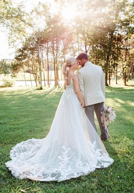 A bride and groom are kissing in a field . the bride is wearing a wedding dress.