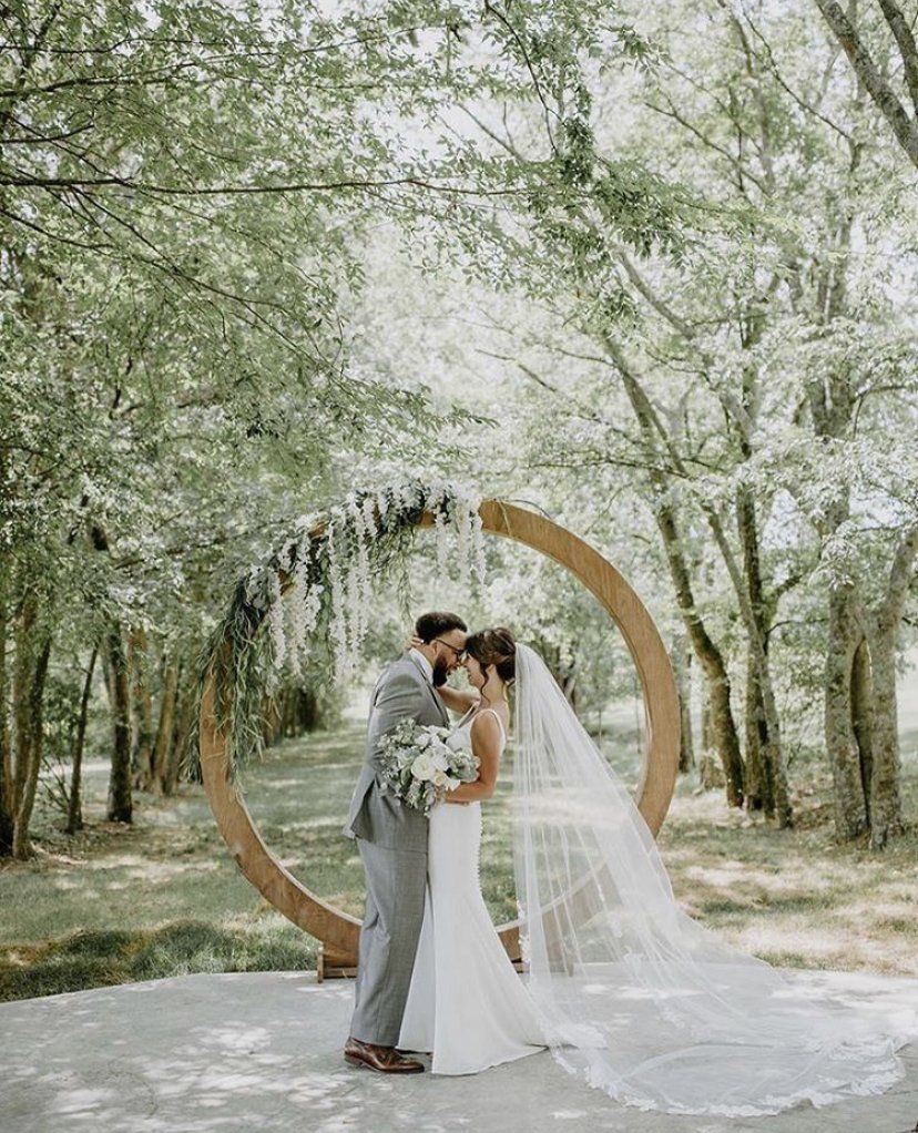 A bride and groom are kissing under a wooden arch in the woods.