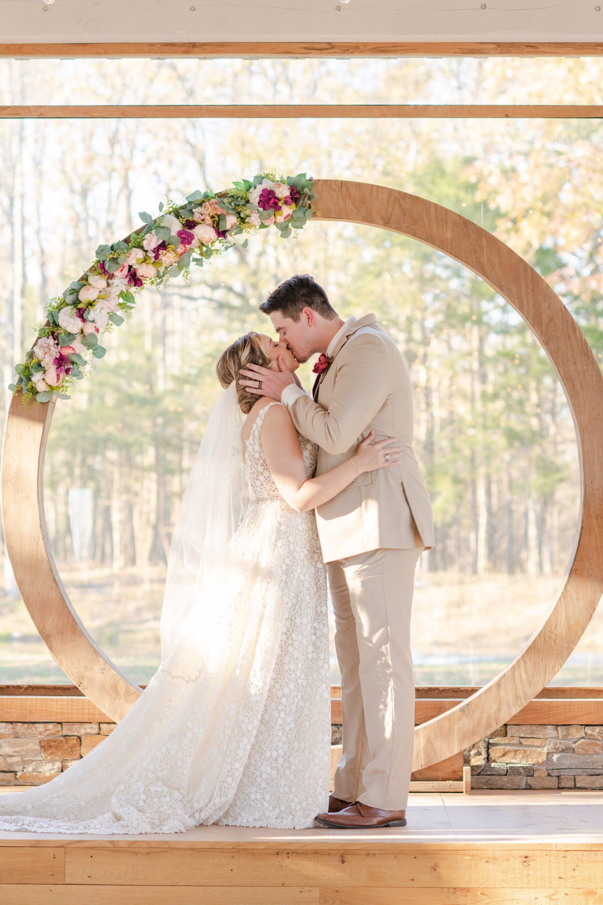A bride and groom are kissing under a wooden arch at their wedding.