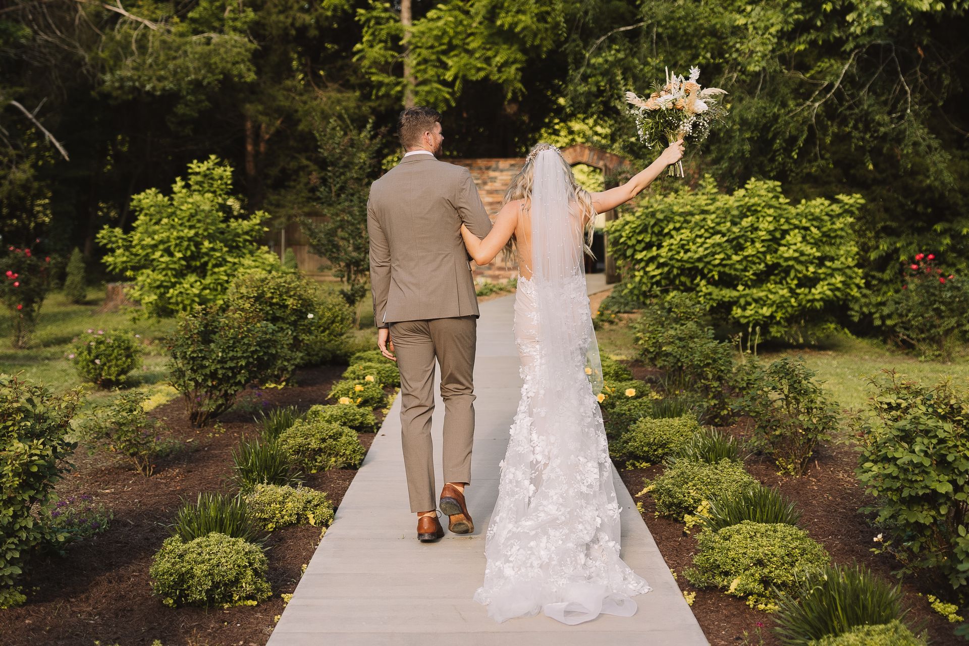 A bride and groom are walking down a path holding hands.
