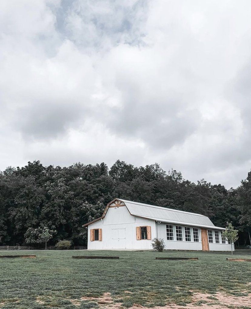 A white barn is sitting in the middle of a grassy field.