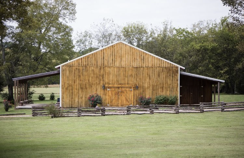 A large wooden barn is sitting in the middle of a grassy field.