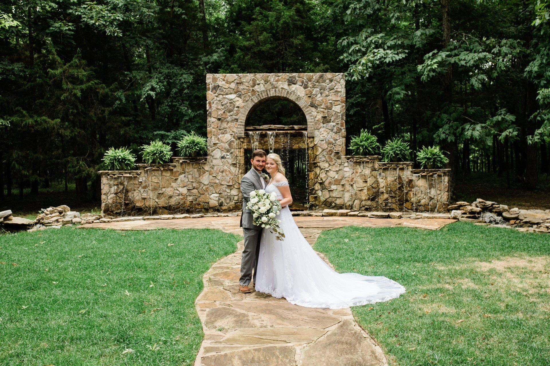 A bride and groom are posing for a picture in front of a stone wall.