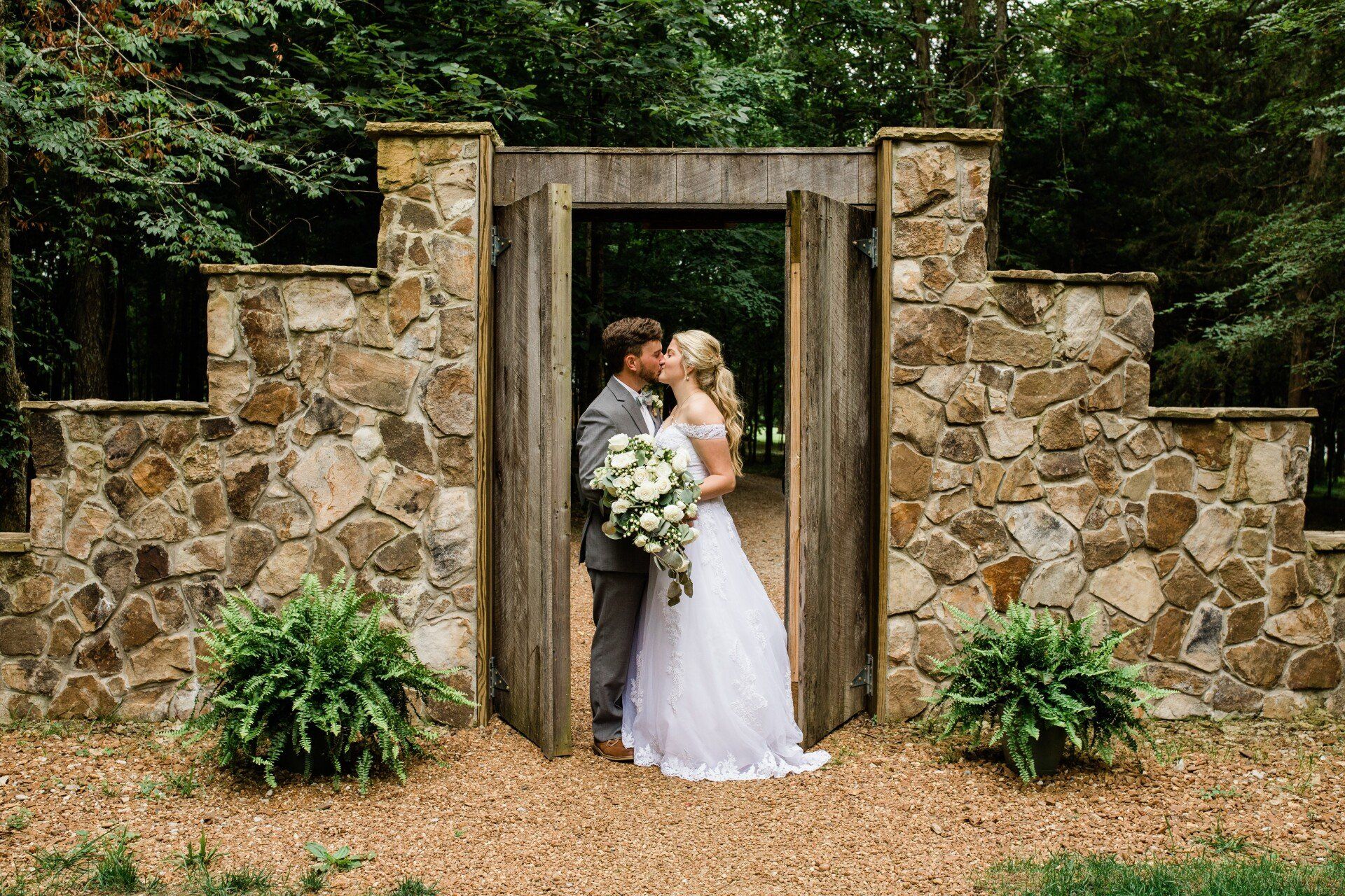 A bride and groom are kissing in front of a stone wall.