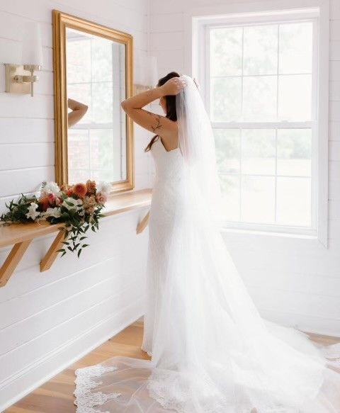a bride in a white dress and veil is standing in front of a mirror .