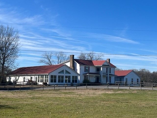 A large white house with a red roof sits in the middle of a grassy field