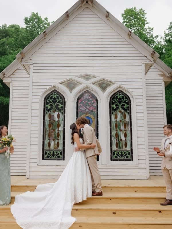 Wedding couple kissing on chapel steps, bride’s white train flowing behind them