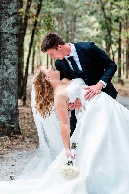 Bride and groom embracing in a forest, with the groom dipping the bride in her white wedding dress