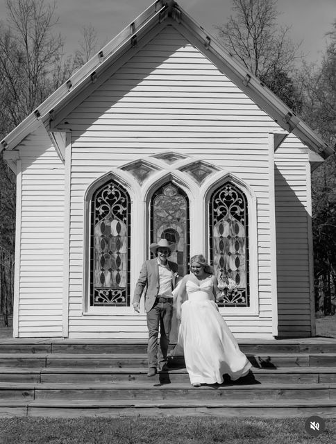 Couple in wedding attire standing on church steps before stained-glass windows