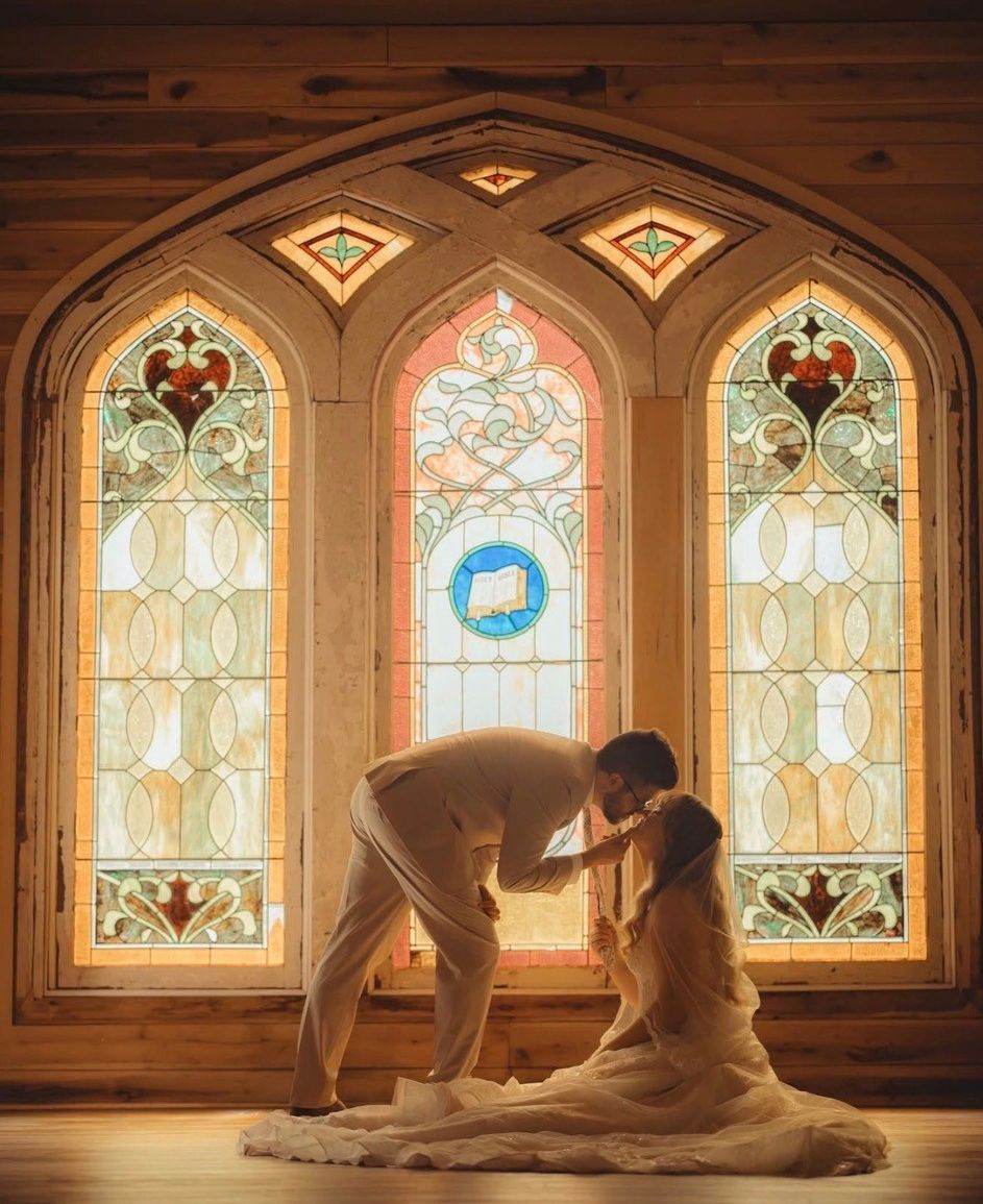 Couple kissing in front of stained-glass windows in a warm, wooden room
