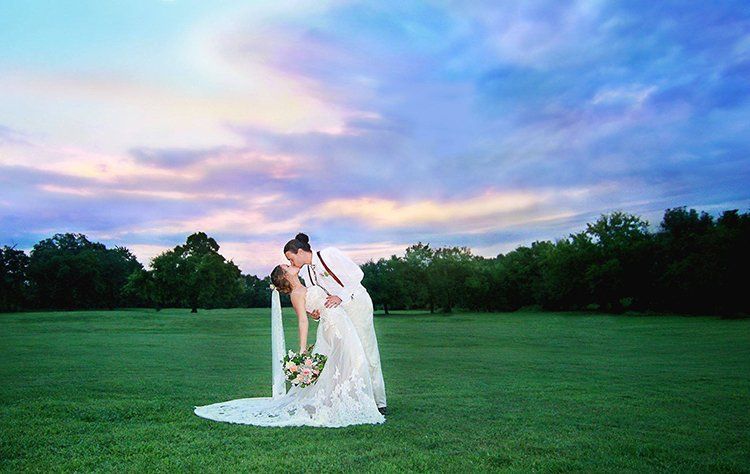 A bride and groom kissing in a field at sunset.