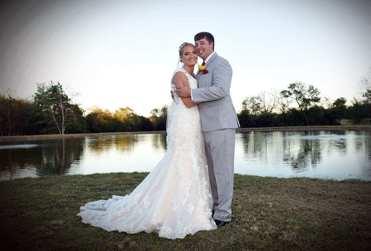 A bride and groom are posing for a picture in front of a lake.