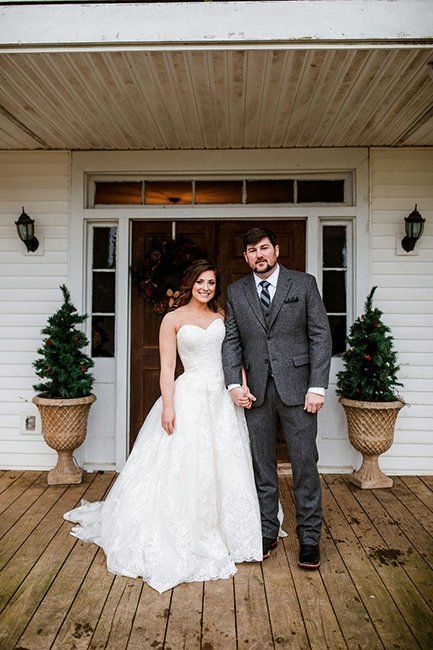 A bride and groom are standing in front of a white house holding hands.
