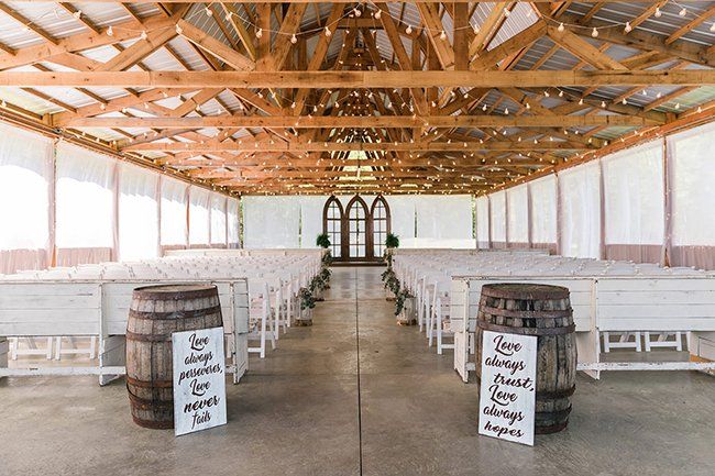 The inside of a barn with barrels and benches for a wedding ceremony.