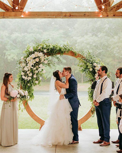 A bride and groom kissing under a wooden arch at their wedding ceremony.