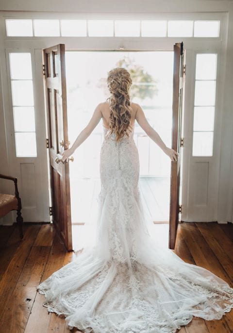 A bride in a wedding dress is standing in front of an open door.