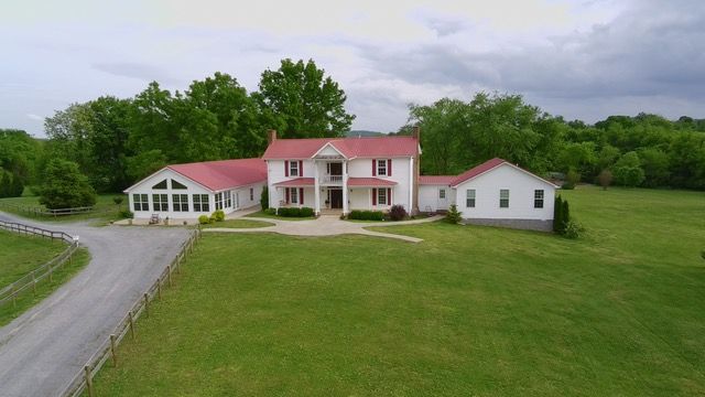 An aerial view of a large white house with a red roof surrounded by trees