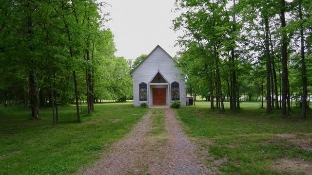 A small white church is surrounded by trees and grass