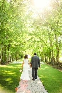 A bride and groom are walking down a path surrounded by trees.
