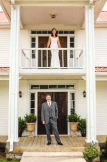 A bride and groom are posing for a picture in front of a large white house.
