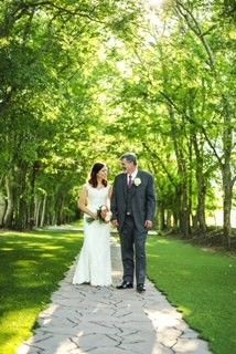 A bride and groom are walking down a path in the woods.