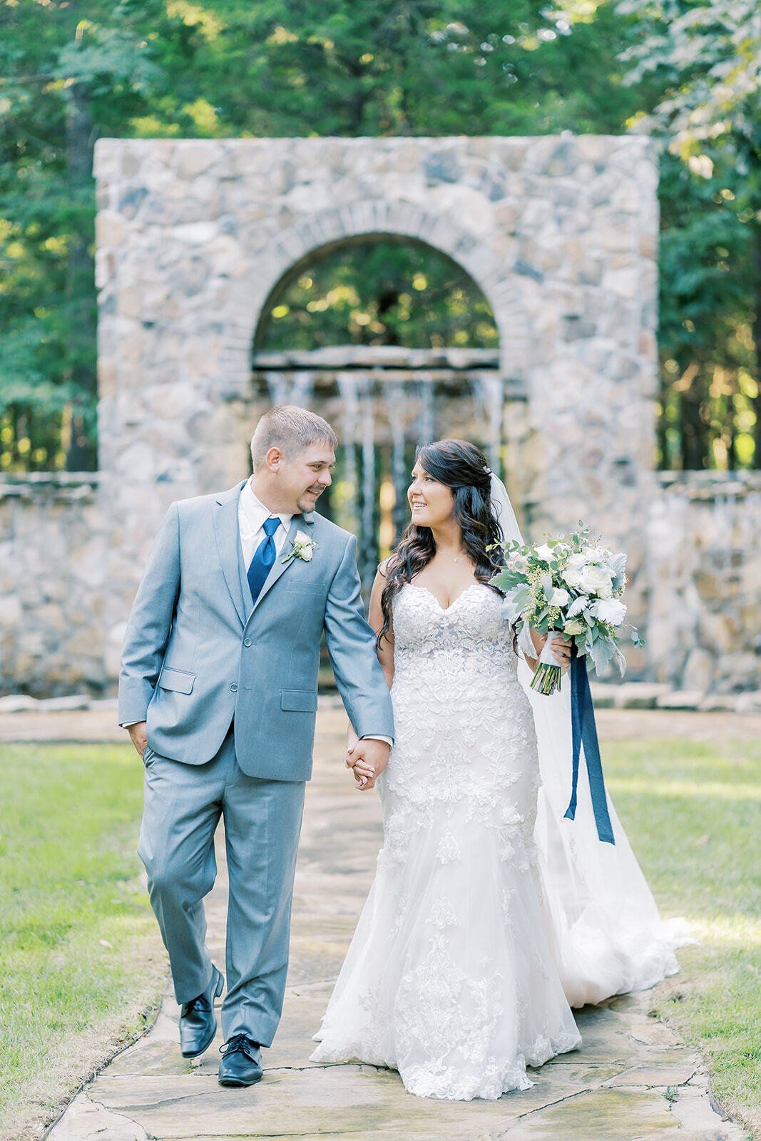 A bride and groom are walking down a path holding hands.