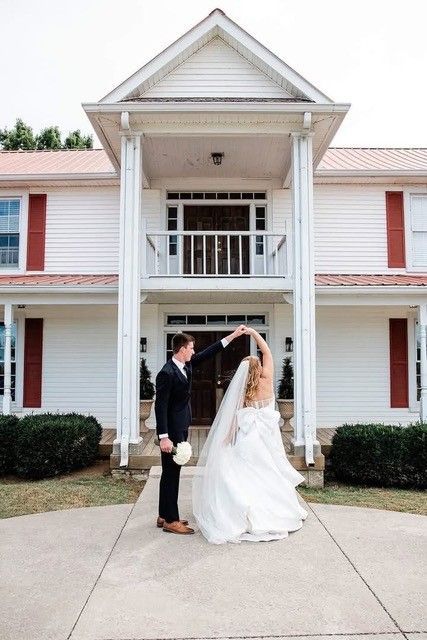 Bride and groom dancing under an arch in front of a white house with columns