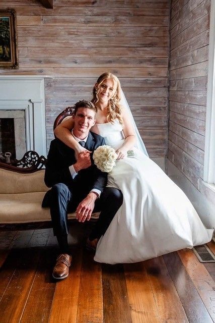 Newlyweds seated together indoors, bride in white gown holding bouquet beside groom in black suit