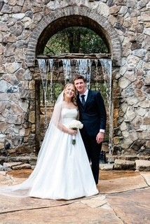 Bride and groom posing under a stone arch waterfall on their wedding day
