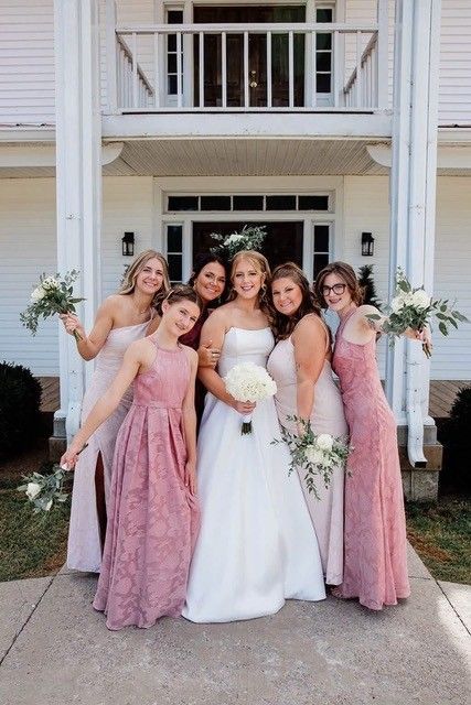 Bride and bridesmaids posing outside a white house, holding bouquets in pink dresses and a white gown