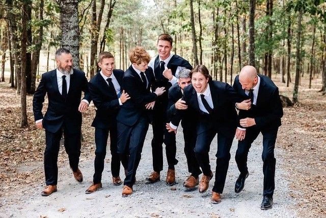 Seven people in suits laughing together on a forest trail