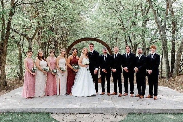 Wedding party posing outdoors on a wooded path, bride in white with bridesmaids in pink and groomsmen in black suits