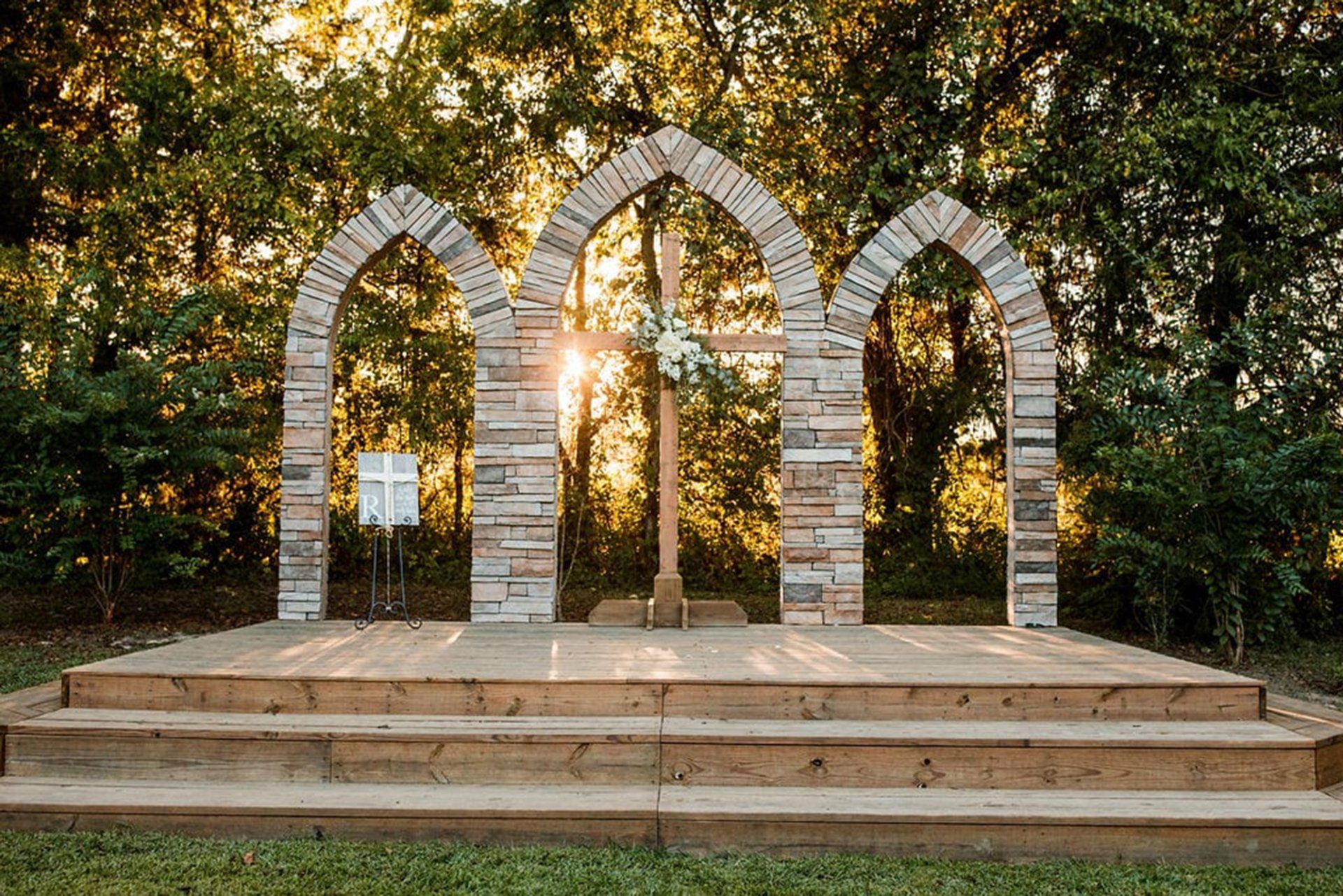 A wooden stage with arches and steps in the middle of a forest.