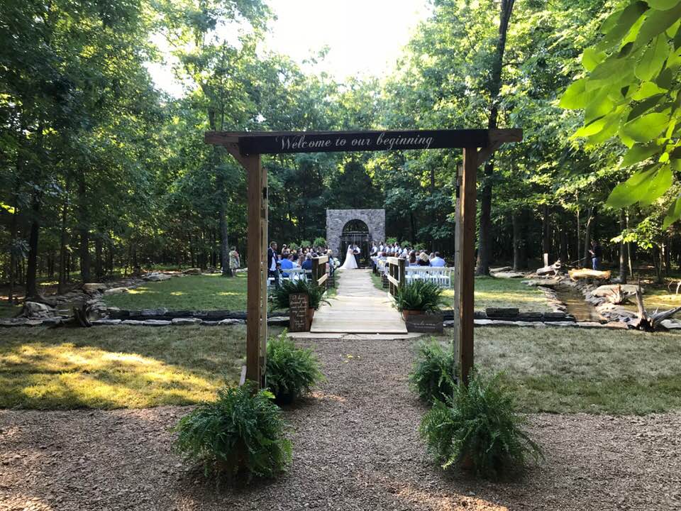 A wooden archway leading to a wedding ceremony in the woods.