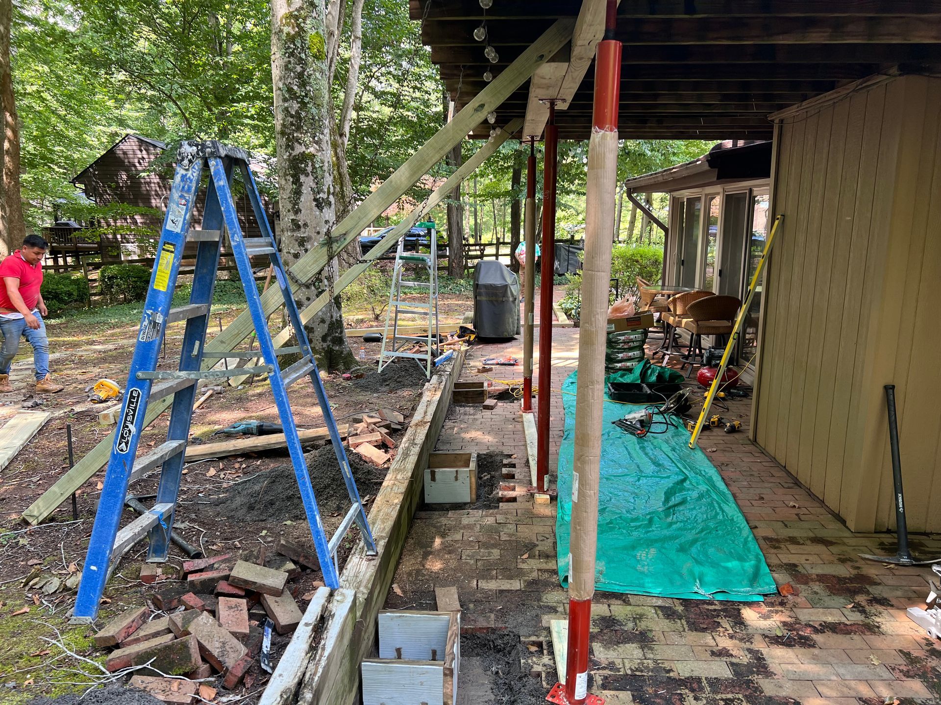A man is standing next to a blue ladder in a yard.