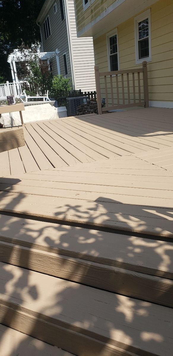 A shadow of a tree is cast on a wooden deck in front of a house.