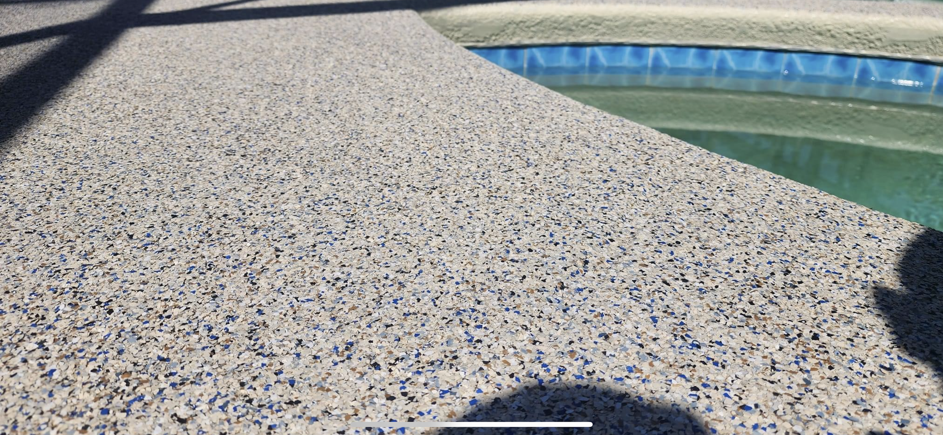 A shadow of a person is cast on a concrete surface next to a pool.