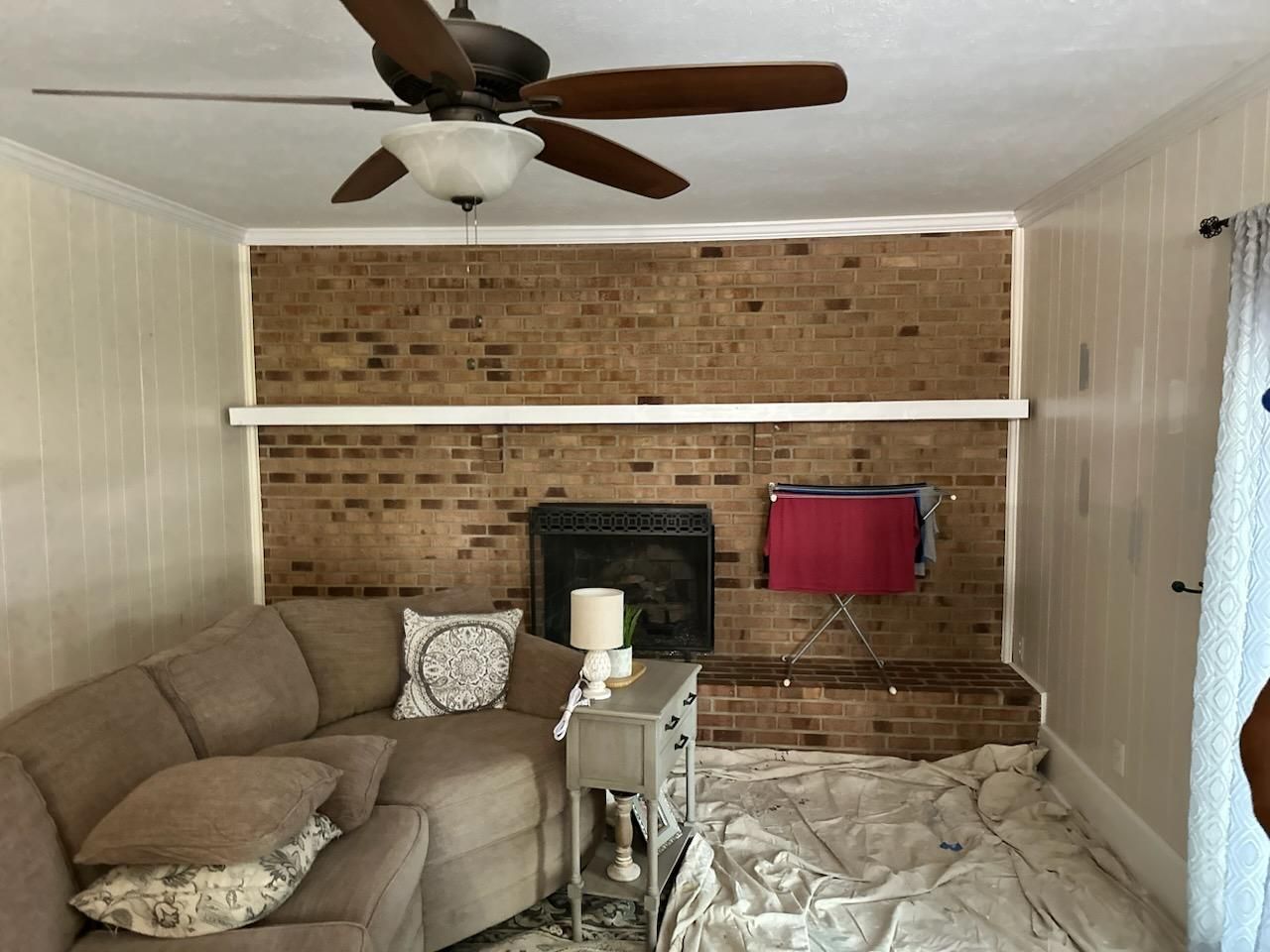 A living room with a fireplace and a ceiling fan before painting job