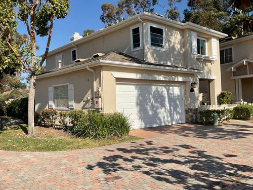 Two-story beige house with white garage door and tiled driveway under sunny trees