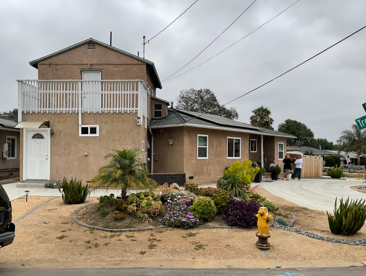 Suburban tan house with balcony, driveway, and landscaped front yard under cloudy sky
