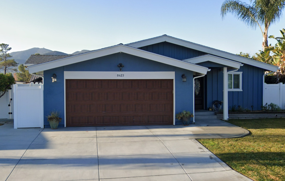 Blue single-story house with a brown garage door, white trim, and a driveway in front