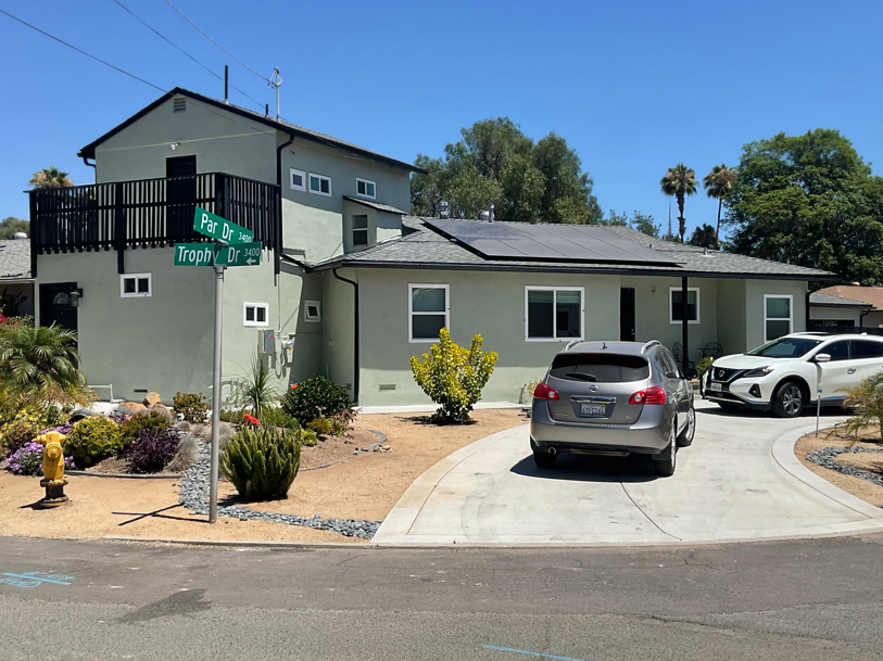 Two-story house with a driveway, parked cars, and desert landscaping on a sunny day