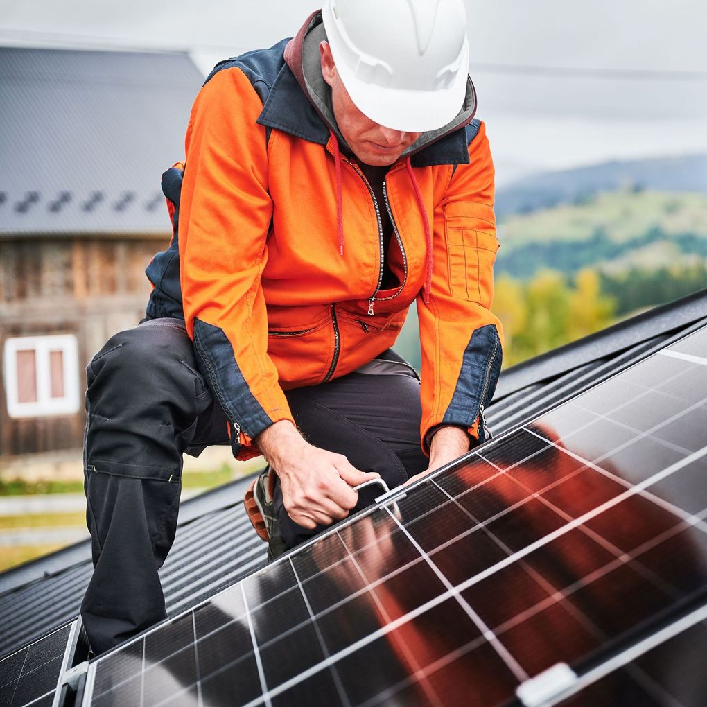 Worker in orange jacket installing solar panels on a roof