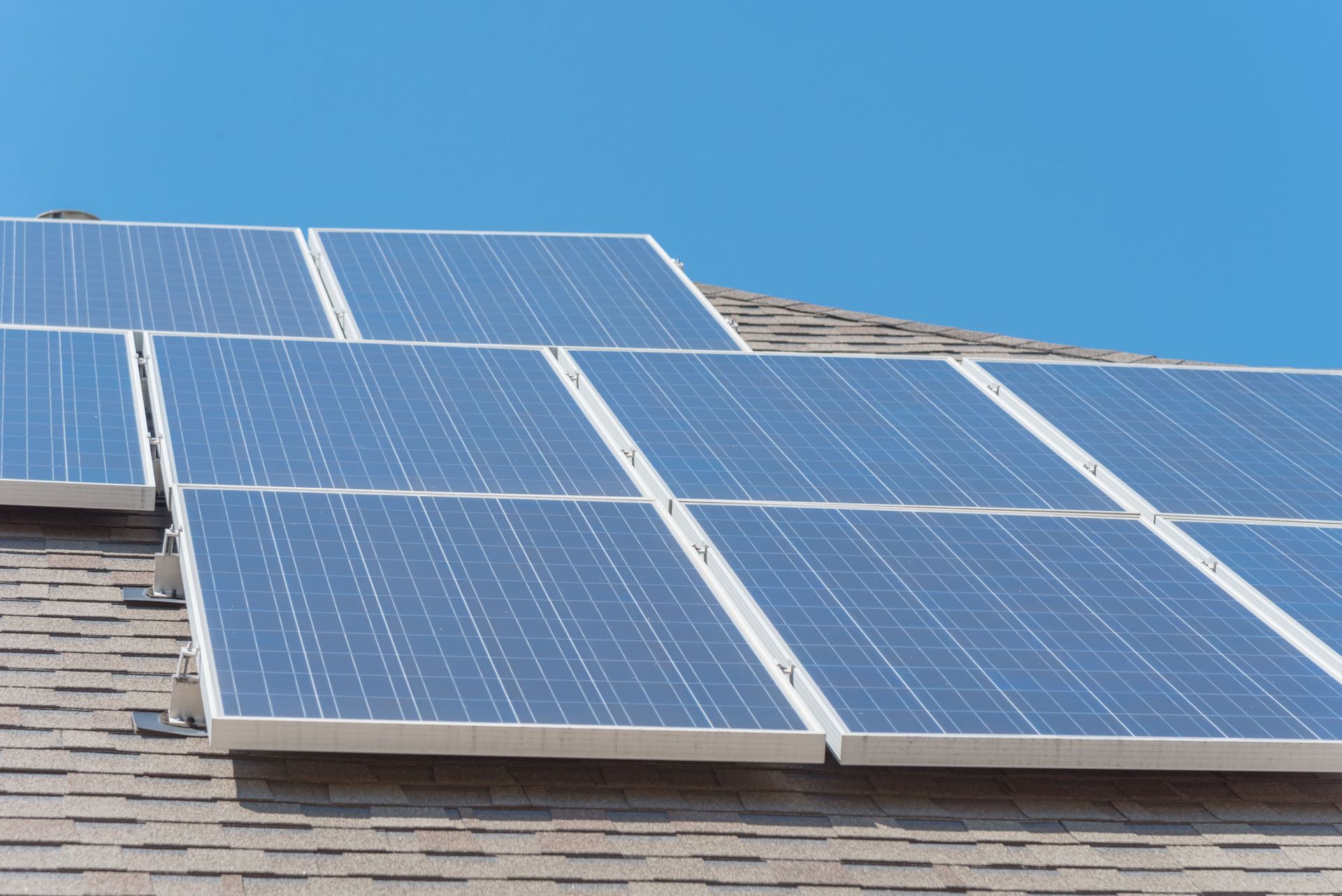 Solar panels installed on a shingled roof under a clear blue sky.